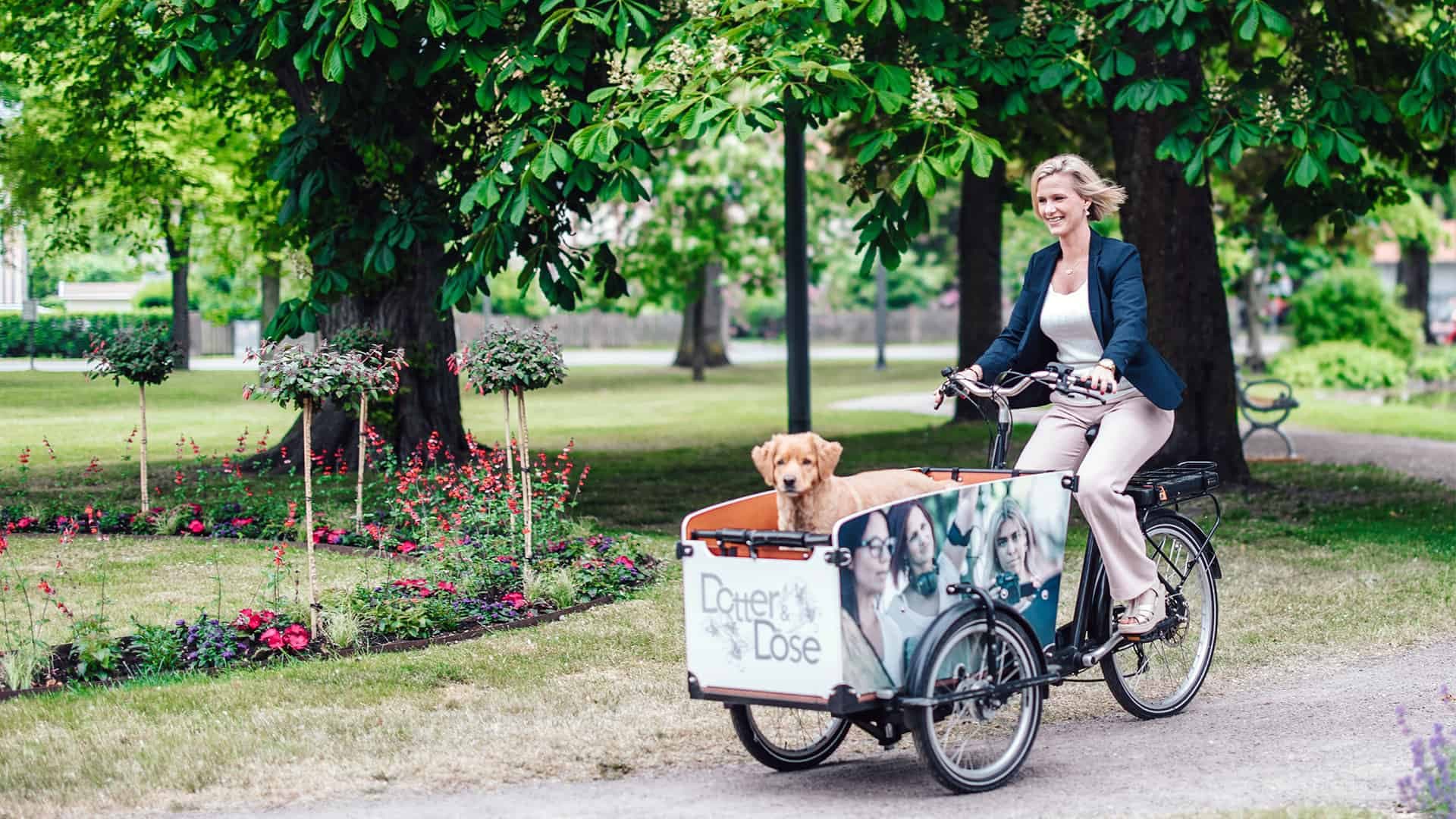 Sandra Torbjörnsdotter cyklar genom en park med en hund framtill.