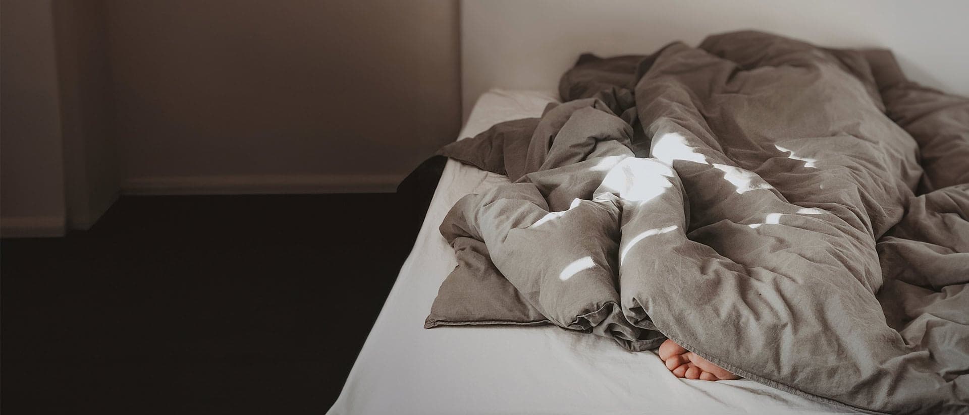 Foto på en säng där man ser en fot stick ut under täcket.