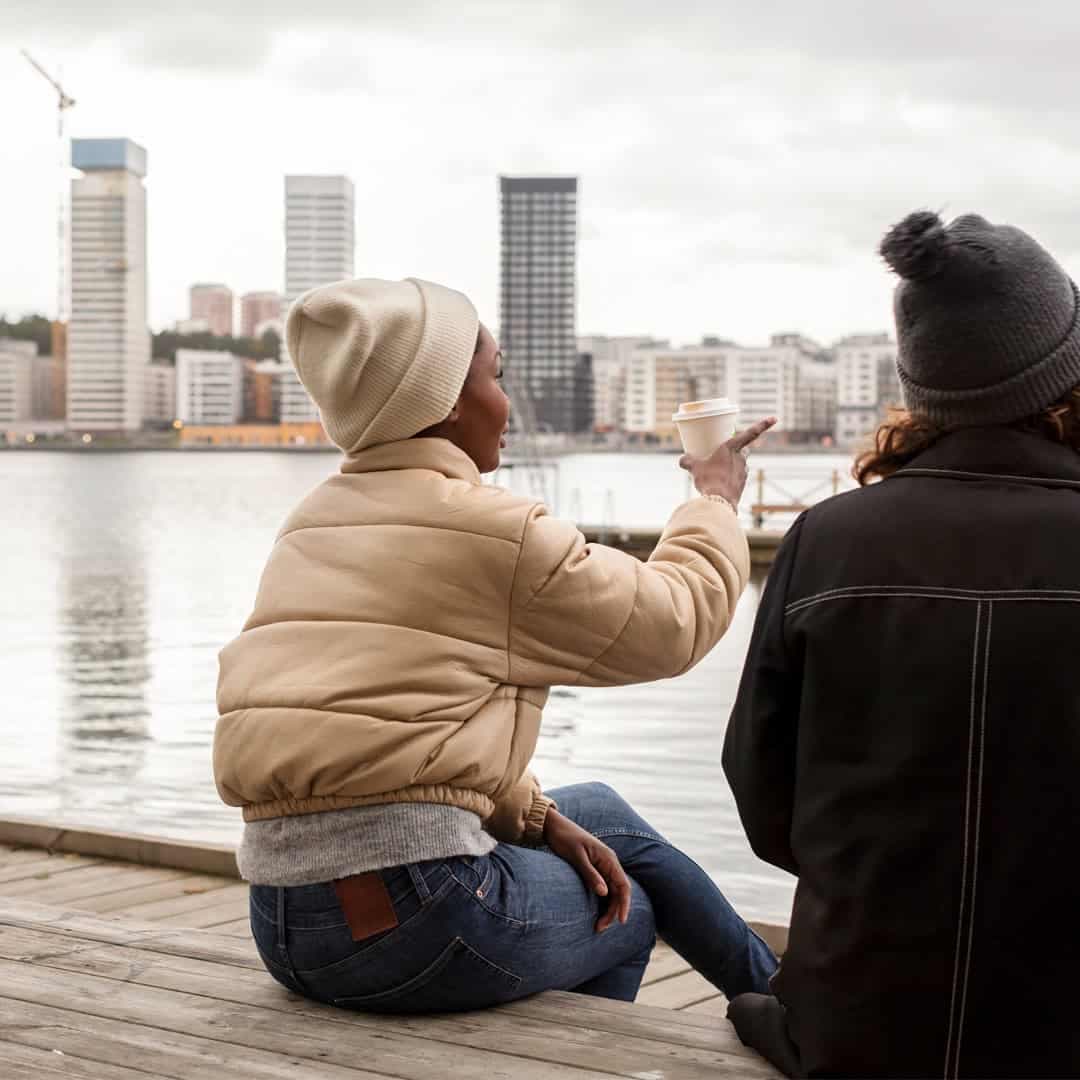 Två personer sitter på en brygga vid vattnet och blickar ut medan de samtalar.